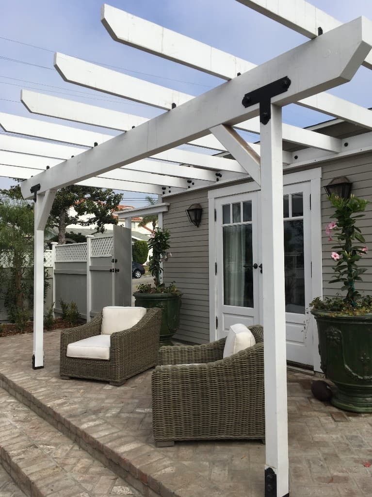 Custom white-painted pergola entry to an accessory dwelling unit, with potted plants and brick patio.