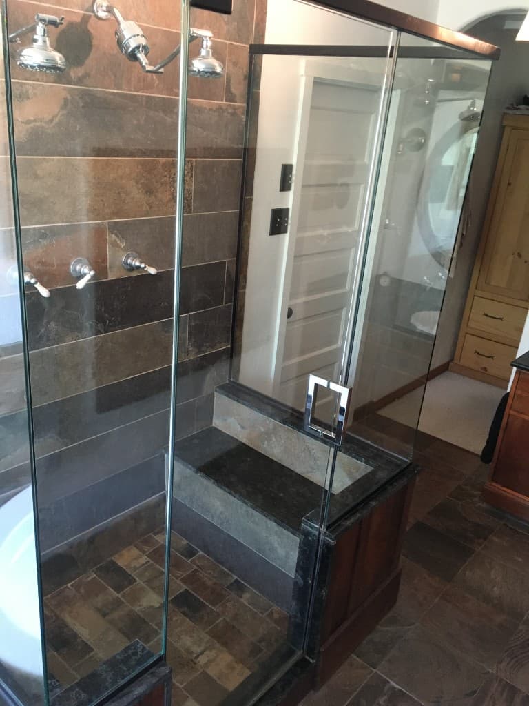 Walk-in shower remodel with horizontal slate stripes, dual rain heads, frameless glass enclosure, and a stone bench seat.